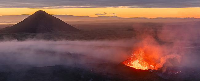 A volcano erupting in front of an orange sky